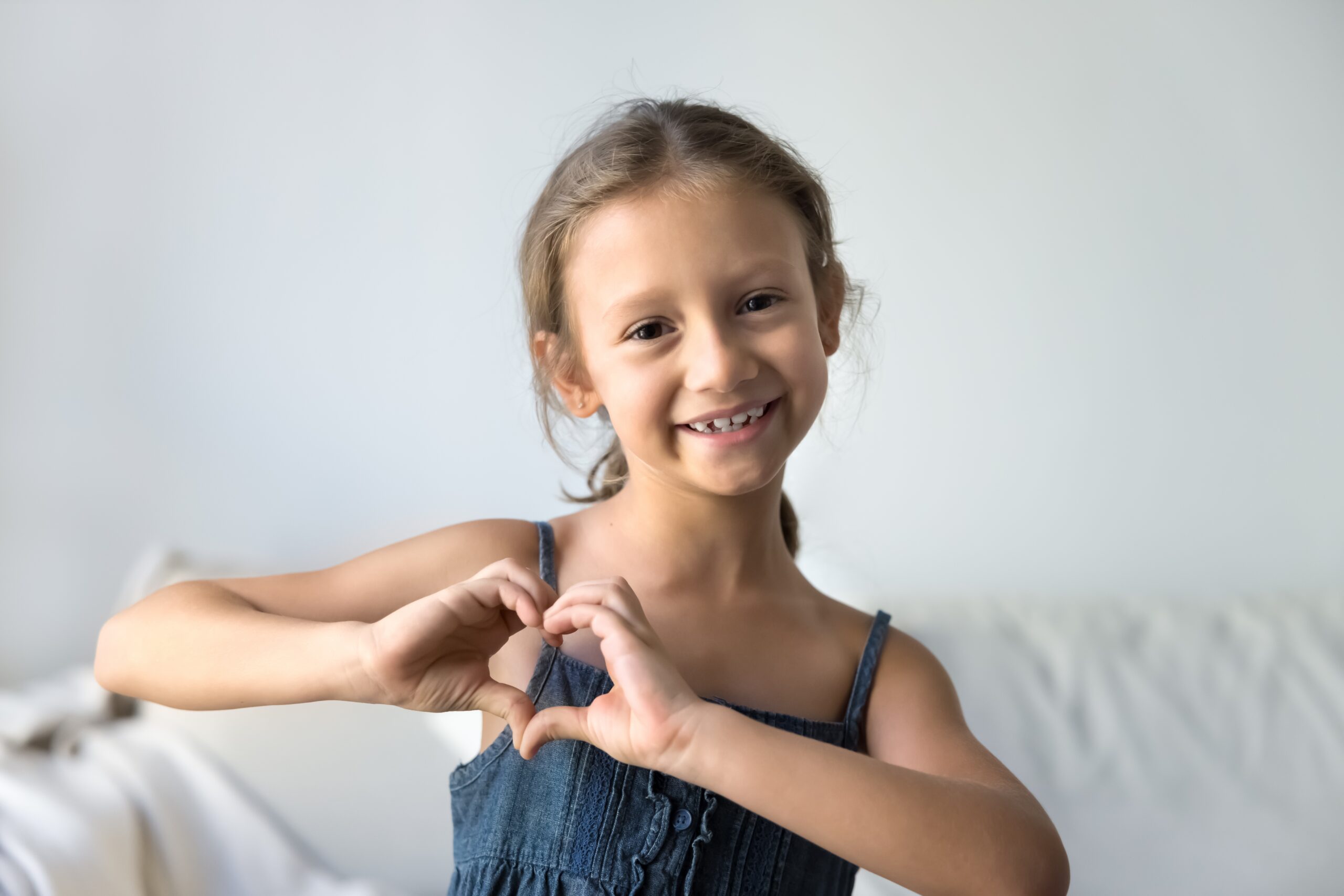 little girl smiling and making a heart with her hands